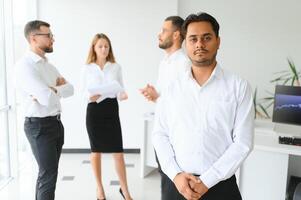 Portrait of smiling indian businessman standing in modern office on colleagues background photo