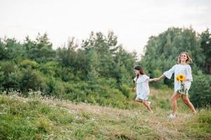 Cheerful mother and her little daughter having fun together in the summer background. Happy family in the nature background. Cute girls with colorful flowers. photo