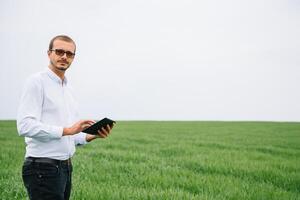Young agronomist holds tablet touch pad computer in green wheat field. Agribusiness concept. agricultural engineer standing in a wheat field with a tablet in summer. photo