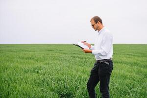 Young agronomist holds tablet touch pad computer in green wheat field. Agribusiness concept. agricultural engineer standing in a wheat field with a tablet in summer photo