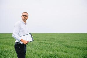Young agronomist holds tablet touch pad computer in green wheat field. Agribusiness concept. agricultural engineer standing in a wheat field with a tablet in summer photo
