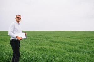 Young agronomist holds tablet touch pad computer in green wheat field. Agribusiness concept. agricultural engineer standing in a wheat field with a tablet in summer photo