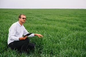 Young agronomist holds tablet touch pad computer in green wheat field. Agribusiness concept. agricultural engineer standing in a wheat field with a tablet in summer. photo