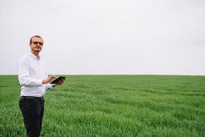 Young agronomist holds tablet touch pad computer in green wheat field. Agribusiness concept. agricultural engineer standing in a wheat field with a tablet in summer. photo