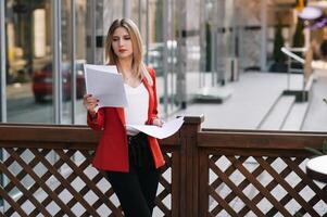 retrato de negocio mujer en sensación de concentrado estrés y ver estar y sostener el papel archivo sábana en el al aire libre peatonal caminar camino con el ciudad espacio de exterior moderno fachada edificio foto