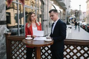 Two confident business colleagues walking on office terrace. Mid adult business man and woman discussing document outdoors on coffee break. Working during break concept. photo
