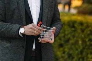 Grocery store chain management, retailing and daily consumer goods trade concept. Business man in a suit with a small miniature shopping cart photo
