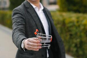 Grocery store chain management, retailing and daily consumer goods trade concept. Business man in a suit with a small miniature shopping cart photo