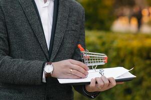 Grocery store chain management, retailing and daily consumer goods trade concept. Business man in a suit with a small miniature shopping cart photo