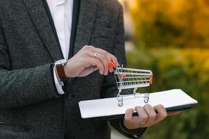 Grocery store chain management, retailing and daily consumer goods trade concept. Business man in a suit with a small miniature shopping cart photo