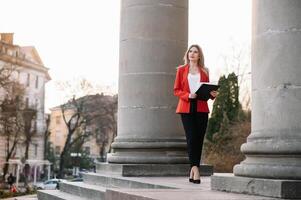 retrato de negocio mujer en sensación de concentrado estrés y ver estar y sostener el papel archivo sábana en el al aire libre peatonal caminar camino con el ciudad espacio de exterior moderno fachada edificio. foto
