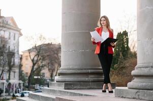 retrato de negocio mujer en sensación de concentrado estrés y ver estar y sostener el papel archivo sábana en el al aire libre peatonal caminar camino con el ciudad espacio de exterior moderno fachada edificio. foto