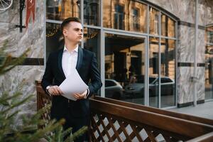 Young business man with documents and mobile phone near of modern building. photo