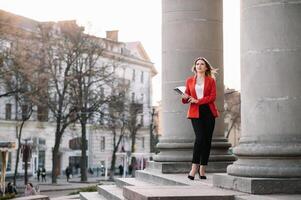 retrato de negocio mujer en sensación de concentrado estrés y ver estar y sostener el papel archivo sábana en el al aire libre peatonal caminar camino con el ciudad espacio de exterior moderno fachada edificio. foto