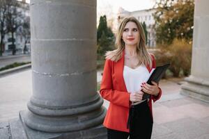 retrato de negocio mujer en sensación de concentrado estrés y ver estar y sostener el papel archivo sábana en el al aire libre peatonal caminar camino con el ciudad espacio de exterior moderno fachada edificio foto