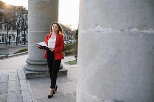 retrato de negocio mujer en sensación de concentrado estrés y ver estar y sostener el papel archivo sábana en el al aire libre peatonal caminar camino con el ciudad espacio de exterior moderno fachada edificio foto