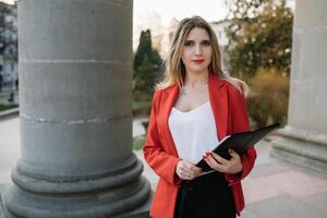retrato de negocio mujer en sensación de concentrado estrés y ver estar y sostener el papel archivo sábana en el al aire libre peatonal caminar camino con el ciudad espacio de exterior moderno fachada edificio. foto