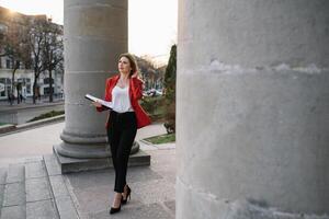 retrato de negocio mujer en sensación de concentrado estrés y ver estar y sostener el papel archivo sábana en el al aire libre peatonal caminar camino con el ciudad espacio de exterior moderno fachada edificio foto