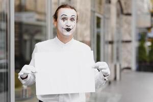 Your text here. Actor mime holding empty white letter. Colorful portrait with gray background. April fools day photo