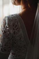 Bride in a apartment in a wedding dress. Bride looks out of the window, wedding day. Charming bride stand in front of window in a white wedding dress. Girl stand by the window at her room. photo