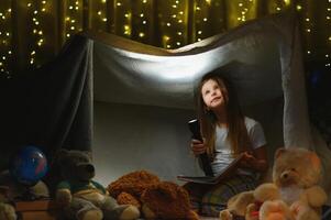 happy child girl laughing and reading book in dark in a tent at home photo