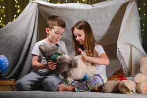 kids lying on floor in cozy nursery. Boy and girl holding flashlights in hands. Children play in a makeshift tent in the nursery. photo