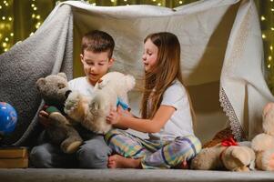 kids lying on floor in cozy nursery. Boy and girl holding flashlights in hands. Children play in a makeshift tent in the nursery. photo