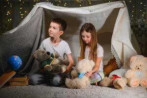 Two little child play at home in the evening to build a camping tent to read books with a flashlight and sleep inside. Concept of game, magic, creativity, alarm systems photo