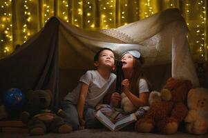 children boy and girl playing and frighten each other with flashlight in tent at night photo
