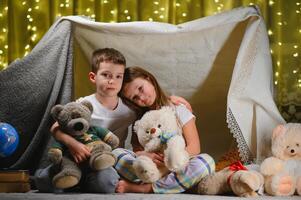 Two little children play at home in the evening to build a camping tent to read books with a flashlight and sleep inside. Concept of game, magic, creativity, alarm systems photo