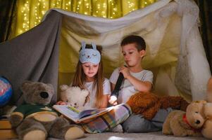 reading and family games in children's tent. boy and girl with book and flashlight before going to bed photo