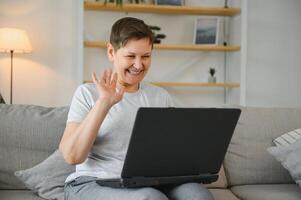 Elderly female sit on couch holding on lap laptop search information, check or typing e-mail, spend time on-line, modern tech, easy interesting pastimes services for retired older generation concept. photo