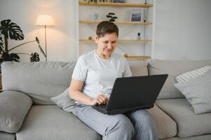 Older mature woman using wireless laptop apps browsing internet sit on sofa, smiling middle aged grandmother working distantly on computer surfing web communicating online looking at screen at home. photo