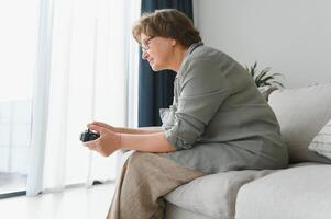 Older person having fun playing a console with a game sitting on the sofa. photo