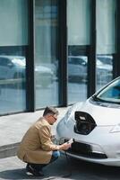 Handsome man using phone while car being charged photo