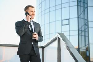 Bearded businessman in formal suit on break using mobile phone use smartphone. business man standing outside on modern urban city street background with coffee cup in downtown outdoors. copy space photo