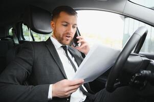 Man of style and status. Handsome young man in full suit smiling while driving a car photo