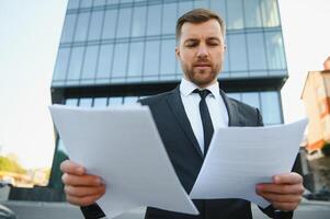 Portrait of young handsome manager wearing suit, holding business documents. photo