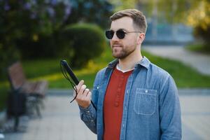 Visually impaired man with walking stick, sitting on bench in city park. Copy space photo