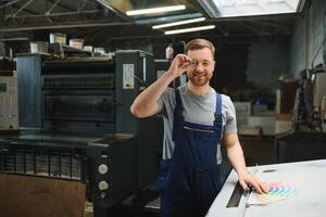 Portrait of production line worker controlling manufacturing process of modern packaging industrial machine in printing factory photo