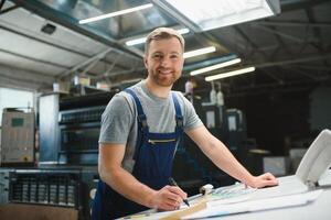 Portrait of production line worker controlling manufacturing process of modern packaging industrial machine in printing factory photo