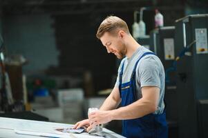 Man worker measuring printing color with spectrometer on the operating desk of the printing plant photo