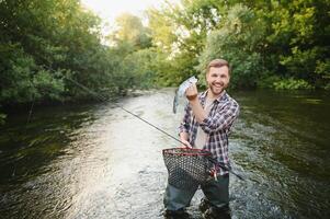 Fisherman catches a trout on the river in summer photo