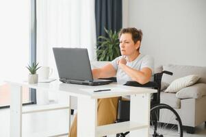 Freelancer in wheelchair using laptop near notebook and papers on table photo