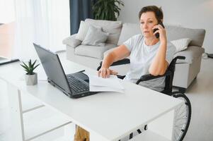 Freelancer in wheelchair using laptop near notebook and papers on table photo