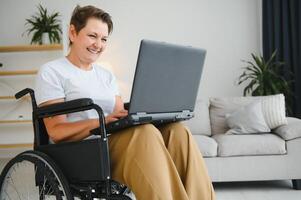 Middle age woman using laptop sitting on wheelchair at home photo