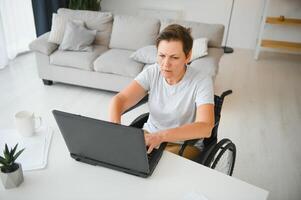 Freelancer in wheelchair using laptop near notebook and papers on table photo