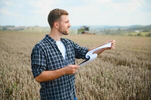 Handsome farmer with tablet standing in front of combine harvester during harvest in field. photo