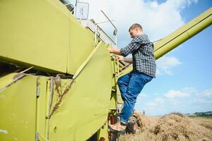 Harvester machine driver climbing into a cab to harvest his wheat field. Farmer getting in combine on ladder holding railing. Agronomist. Rancher after harvesting work photo