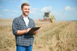 Handsome farmer with tablet standing in front of combine harvester during harvest in field. photo